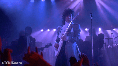 A Man Is Playing A Guitar And Singing Into A Microphone On A Stage . GIF