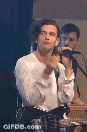A Man Is Playing A Guitar And Singing Into A Microphone . GIF