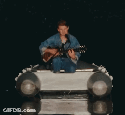 A Man Is Playing A Guitar And Singing Into A Microphone GIF