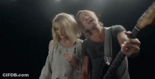 A Man Is Playing A Guitar And Singing Into A Microphone While A Woman Stands Behind Him . GIF
