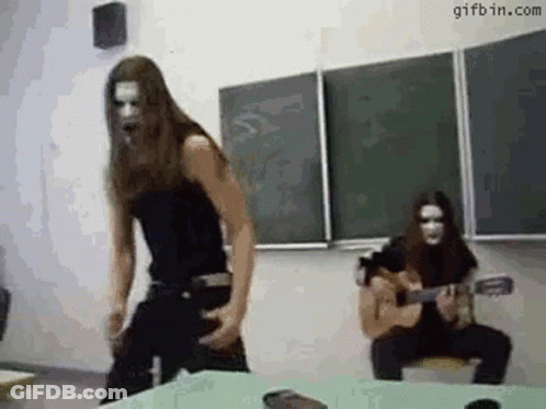 A Man Is Playing A Guitar In A Classroom And A Woman Is Dancing . GIF