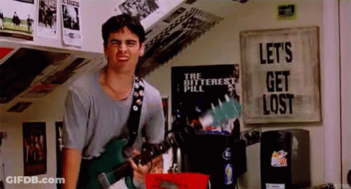 A Man Is Playing A Guitar In A Room With A Poster That Says Let 'S Get Lost . GIF