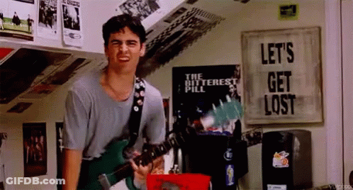 A Man Is Playing A Guitar In A Room With A Sign That Says Let 'S Get Lost GIF