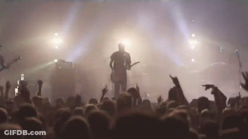 A Man Is Playing A Guitar In Front Of A Crowd Of People GIF