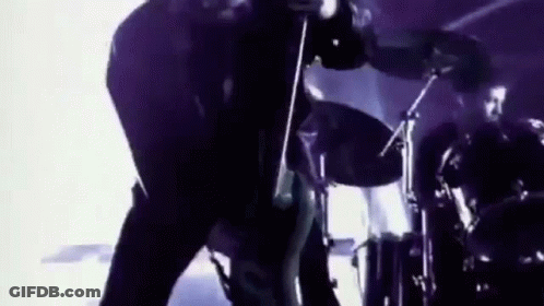 A Man Is Playing A Guitar In Front Of A Drum Set . GIF