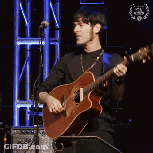 A Man Is Playing A Guitar In Front Of A Microphone With A Laurel Wreath On It GIF