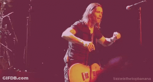 A Man Is Playing A Guitar In Front Of A Microphone With The Words Lizzie Is The Topbanana Written Below Him GIF