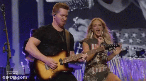 A Man Is Playing A Guitar Next To A Woman Who Is Singing Into A Microphone . GIF