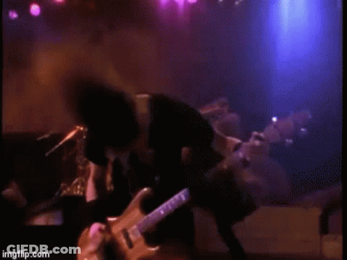 A Man Is Playing A Guitar On A Stage In A Dark Room . GIF