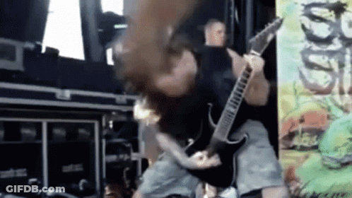 A Man Is Playing A Guitar On A Stage While A Woman Holds His Head . GIF