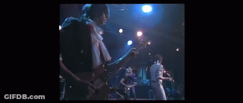 A Man Is Playing A Guitar On A Stage While Another Man Sings Into A Microphone . GIF