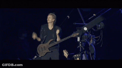 A Man Is Playing A Guitar On A Stage With A Camera Behind Him GIF