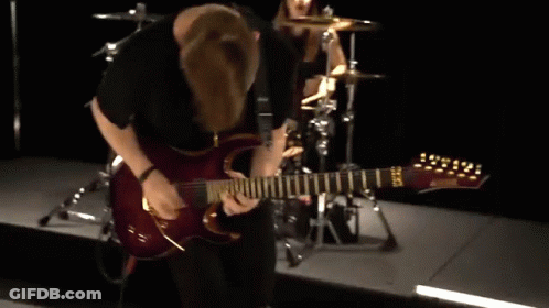 A Man Is Playing A Guitar On A Stage With A Drummer In The Background GIF