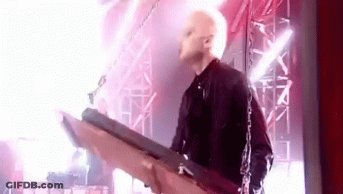 A Man Is Playing A Guitar On A Stage With Chains Around Him . GIF