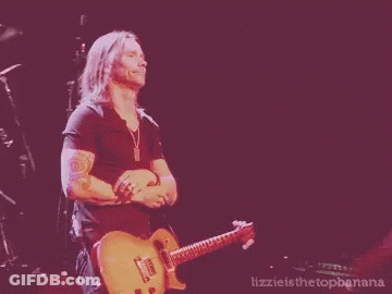 A Man Is Playing A Guitar On A Stage With The Words Lizzie Is The Topbanana Below Him GIF