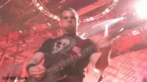 A Man Is Playing A Guitar On Stage In A Dark Room . GIF