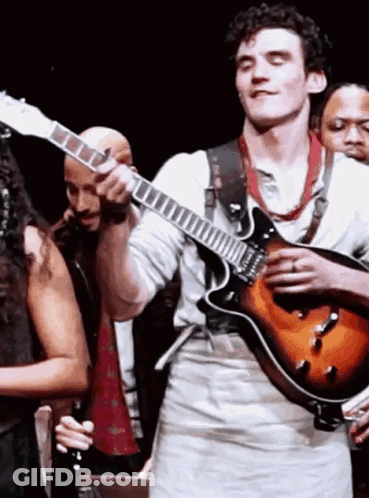 A Man Is Playing A Guitar On Stage In Front Of A Group Of People GIF