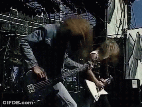 A Man Is Playing A Guitar On Stage While Another Man Drums . GIF