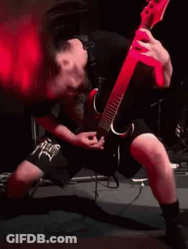 A Man Is Playing A Guitar On Stage With Red Smoke Coming Out Of His Mouth . GIF