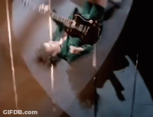 A Man Is Playing A Guitar Upside Down On A Skateboard . GIF