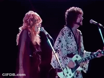 A Man Is Playing A Guitar While A Woman Sings Into A Microphone On Stage . GIF