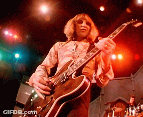 A Man Is Playing A Guitar With The Letter G On The Neck GIF