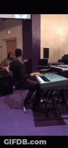 A Man Is Playing A Keyboard In A Room With An Exit Sign On The Wall GIF