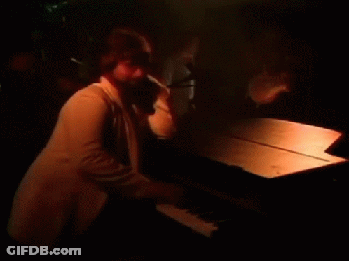 A Man Is Playing A Piano In A Dark Room With A Microphone In The Background . GIF