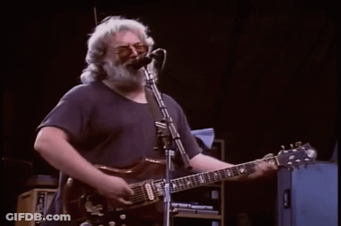 A Man Is Playing A Piano On A Stage While A Band Plays Behind Him . GIF