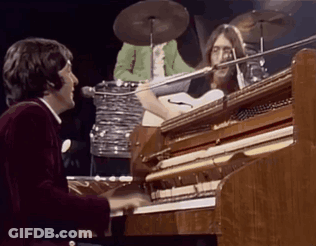 A Man Is Playing A Piano On Stage While A Drummer Plays Drums Behind Him . GIF