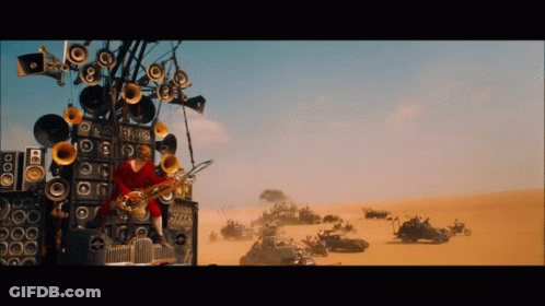 A Man Is Playing A Saxophone In Front Of A Wall Of Speakers In The Desert GIF