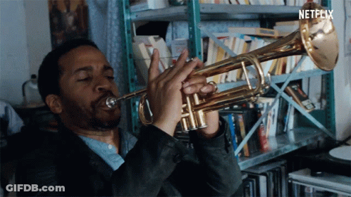 A Man Is Playing A Trumpet In Front Of A Shelf With Netflix Written On The Bottom GIF