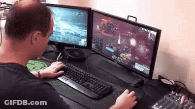 A Man Is Playing A Video Game On Two Monitors . GIF