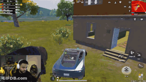 A Man Is Playing A Video Game With A Car In The Background GIF