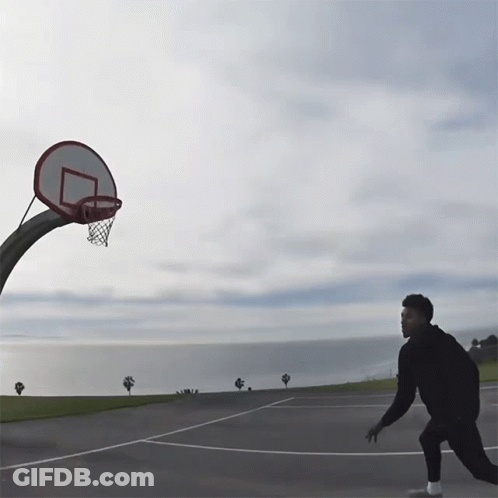 A Man Is Playing Basketball In Front Of A Basketball Hoop With The Ocean In The Background GIF