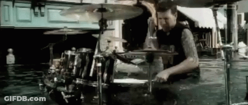 A Man Is Playing Drums In A Room Filled With Water . GIF