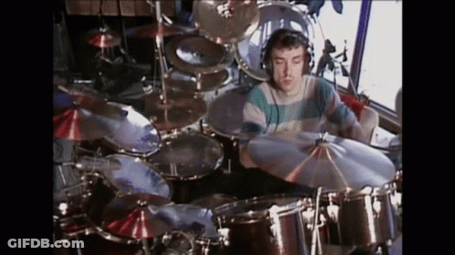 A Man Is Playing Drums In A Room With A Lot Of Drums And Cymbals . GIF