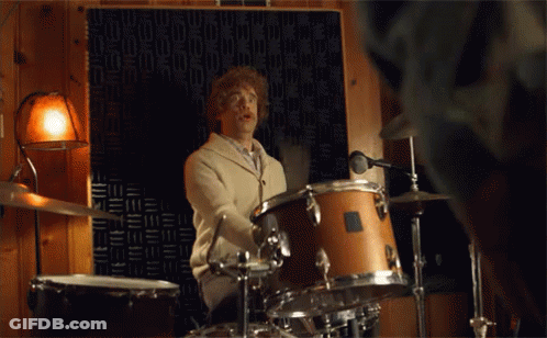 A Man Is Playing Drums In A Room With A Microphone GIF