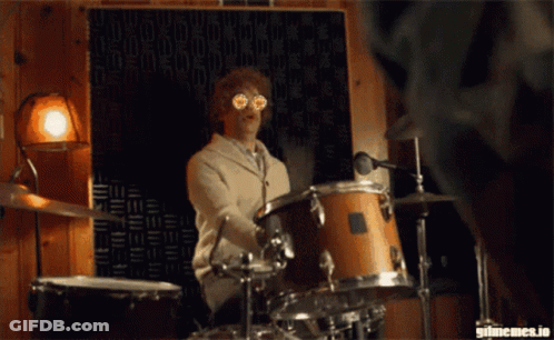 A Man Is Playing Drums In Front Of A Wall That Says Gifmemes.io On It GIF