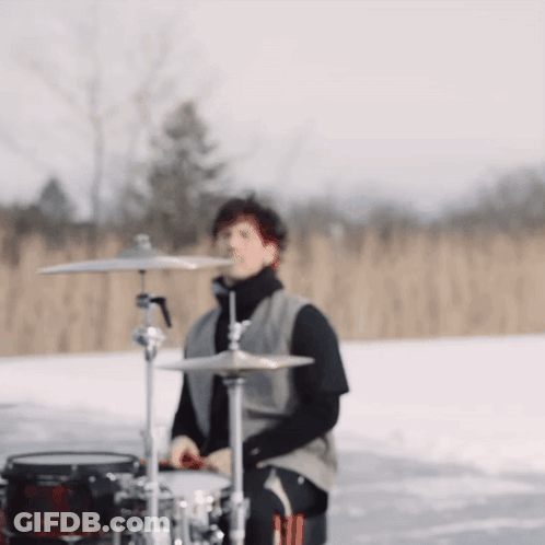 A Man Is Playing Drums In The Snow In A Field GIF