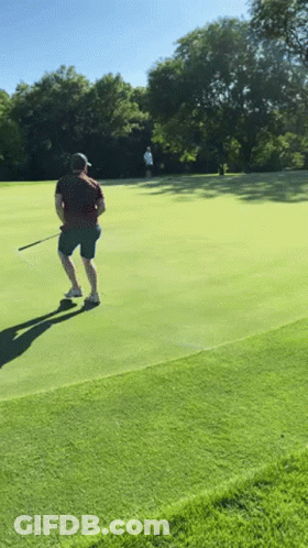 A Man Is Playing Golf On A Lush Green Course GIF