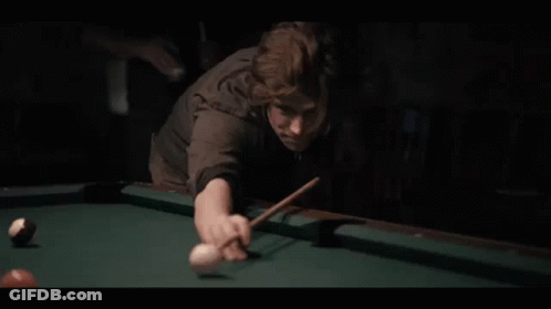 A Man Is Playing Pool In A Dark Room With A Pool Cue And Ball . GIF