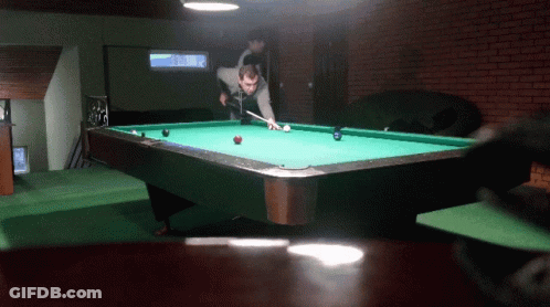 A Man Is Playing Pool In A Room With A Brick Wall GIF