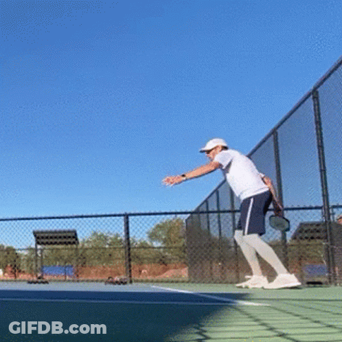 A Man Is Playing Tennis On A Court With A Blue Sky In The Background GIF