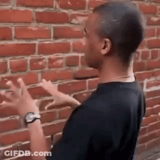 A Man Is Pointing At A Brick Wall While Wearing A Watch . GIF