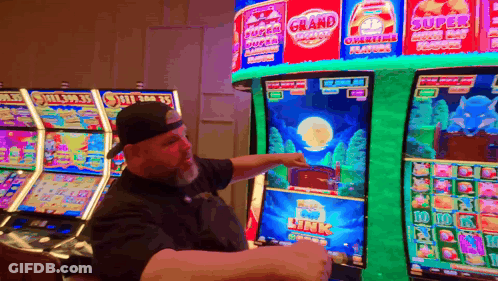 A Man Is Pointing At A Slot Machine That Has The Word Grand On It GIF