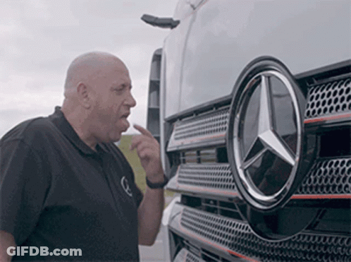 A Man Is Pointing At The Mercedes Logo On The Front Of A Truck . GIF