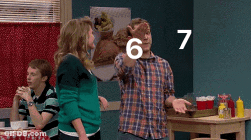 A Man Is Pointing At The Number 7 While Standing Next To A Woman GIF
