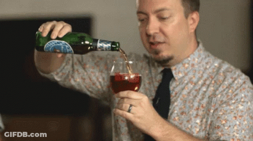 A Man Is Pouring A Drink From A Bottle Into A Glass With A Blue Label That Says ' A ' On It GIF