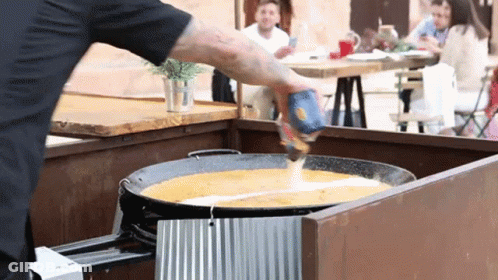 A Man Is Pouring Sauce Into A Pan With A Can Of Salsa GIF